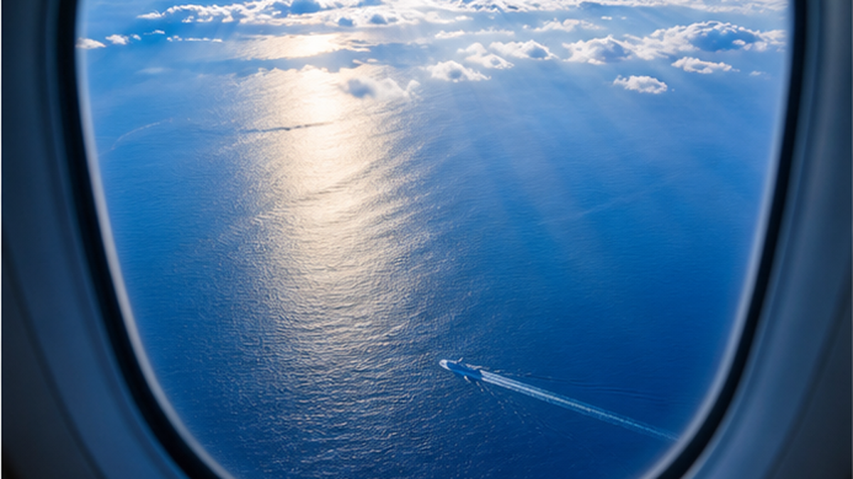 空から見た青い海と、そこへ伸びる飛行機の影のイメージ